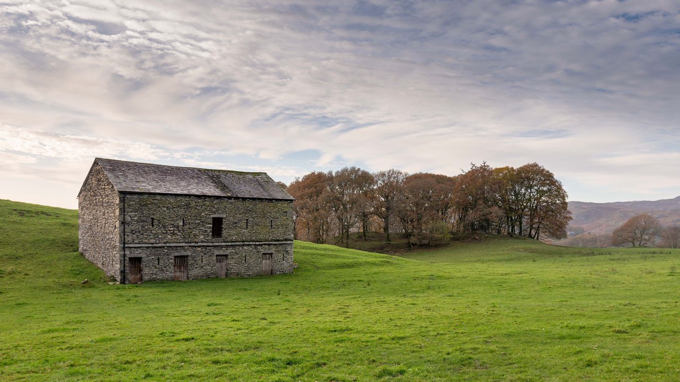 A barn in green fields, with trees and hills behind.